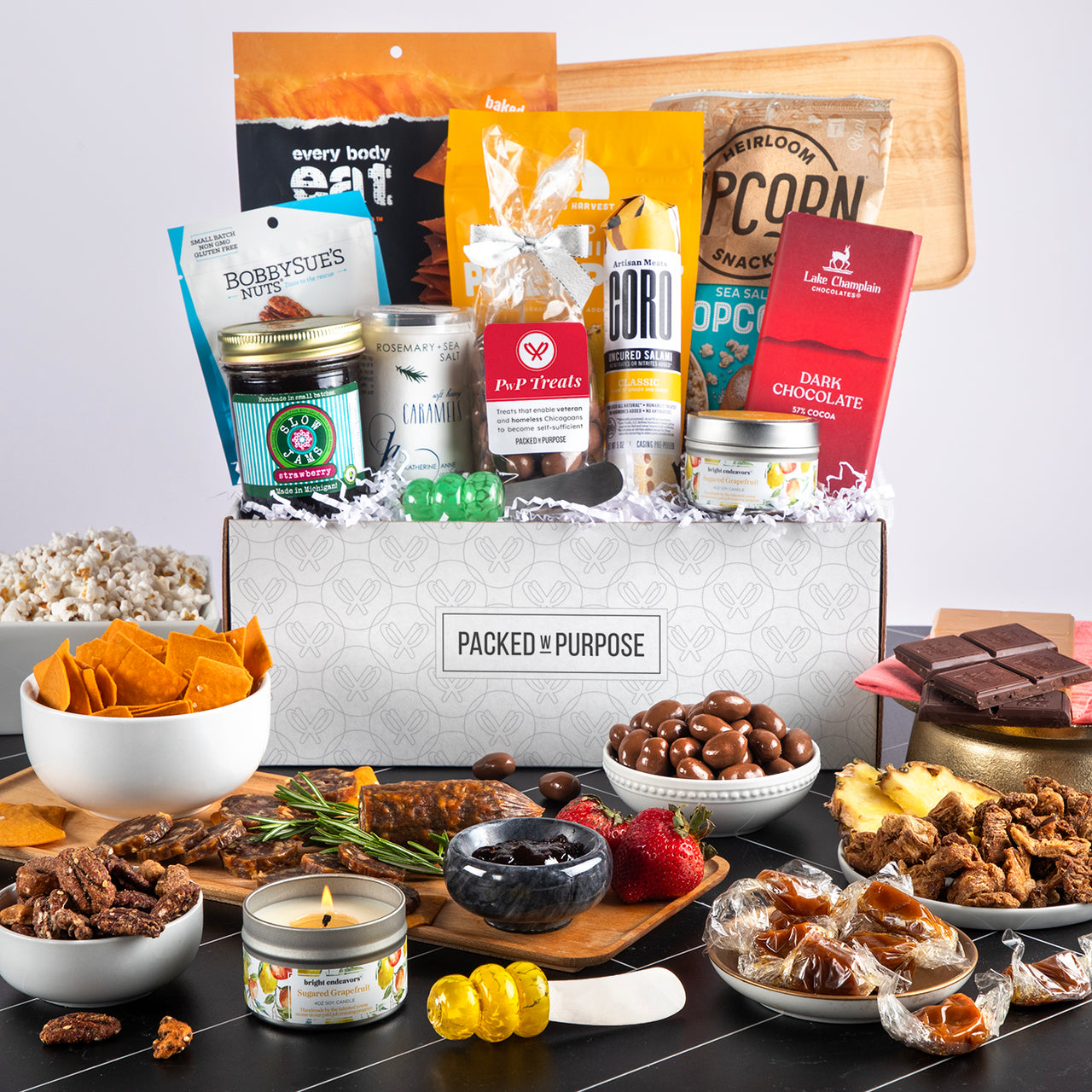 Charcuterie gift set labeled ‘Deluxe Charcuterie Board’ with preserves, salami, almonds, crackers, and tapenade.