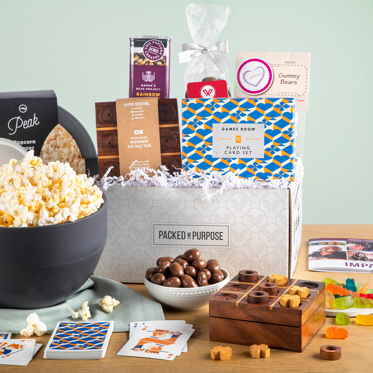 Open gift box labeled ‘Family Fun & Movie Night’ with rainbow popcorn kit, trivia cards, cookies, and chocolate almonds.