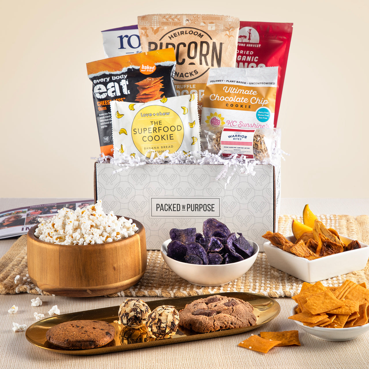 Open gift box labeled ‘Gluten & Nut-Free Vegan Treats’ with dark chocolate, veggie chips, cookies, and dried mango.