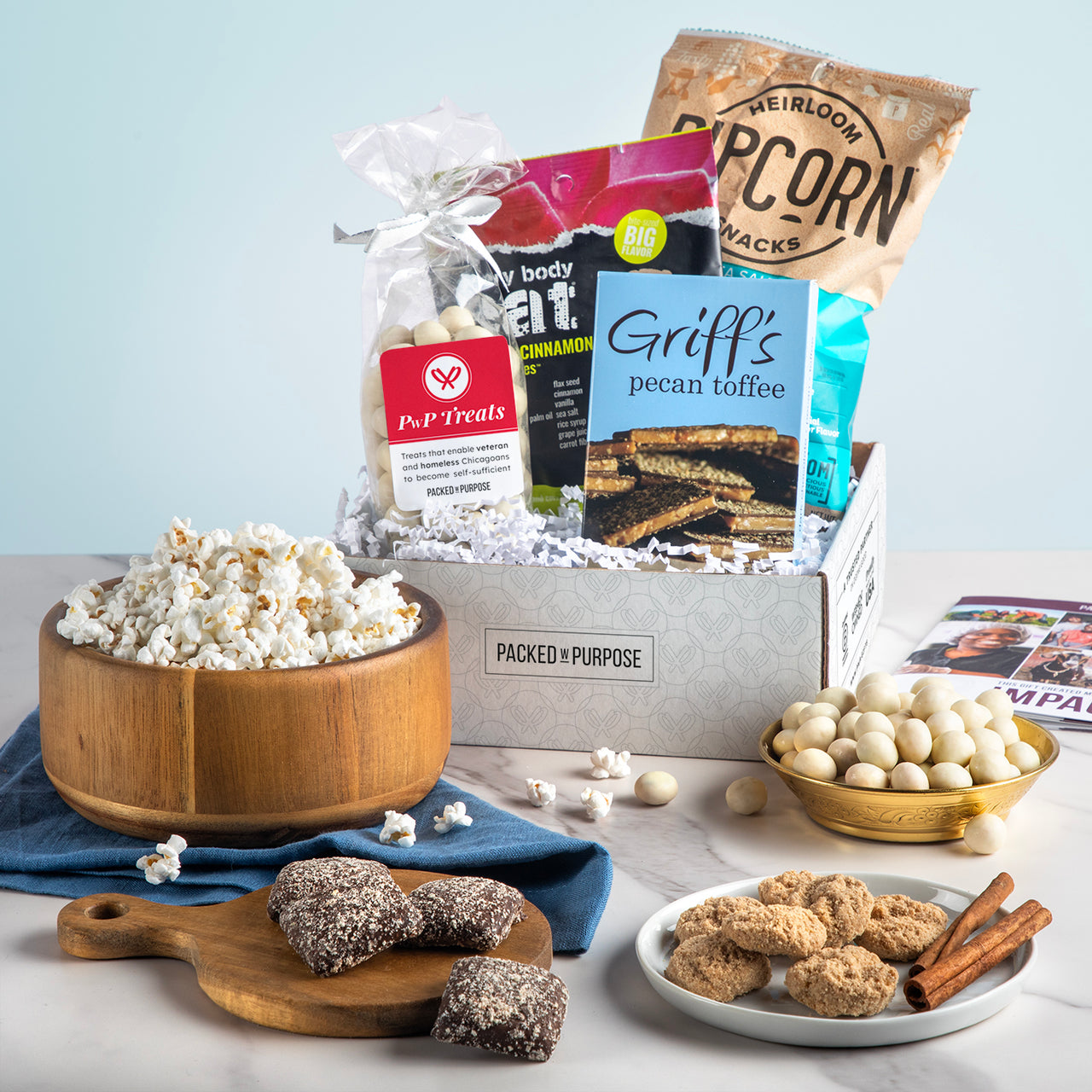 Open gift basket labeled ‘Petite & Perfect’ with toffee, chocolate chip cookies, sea salt popcorn, and chocolate meltaways.