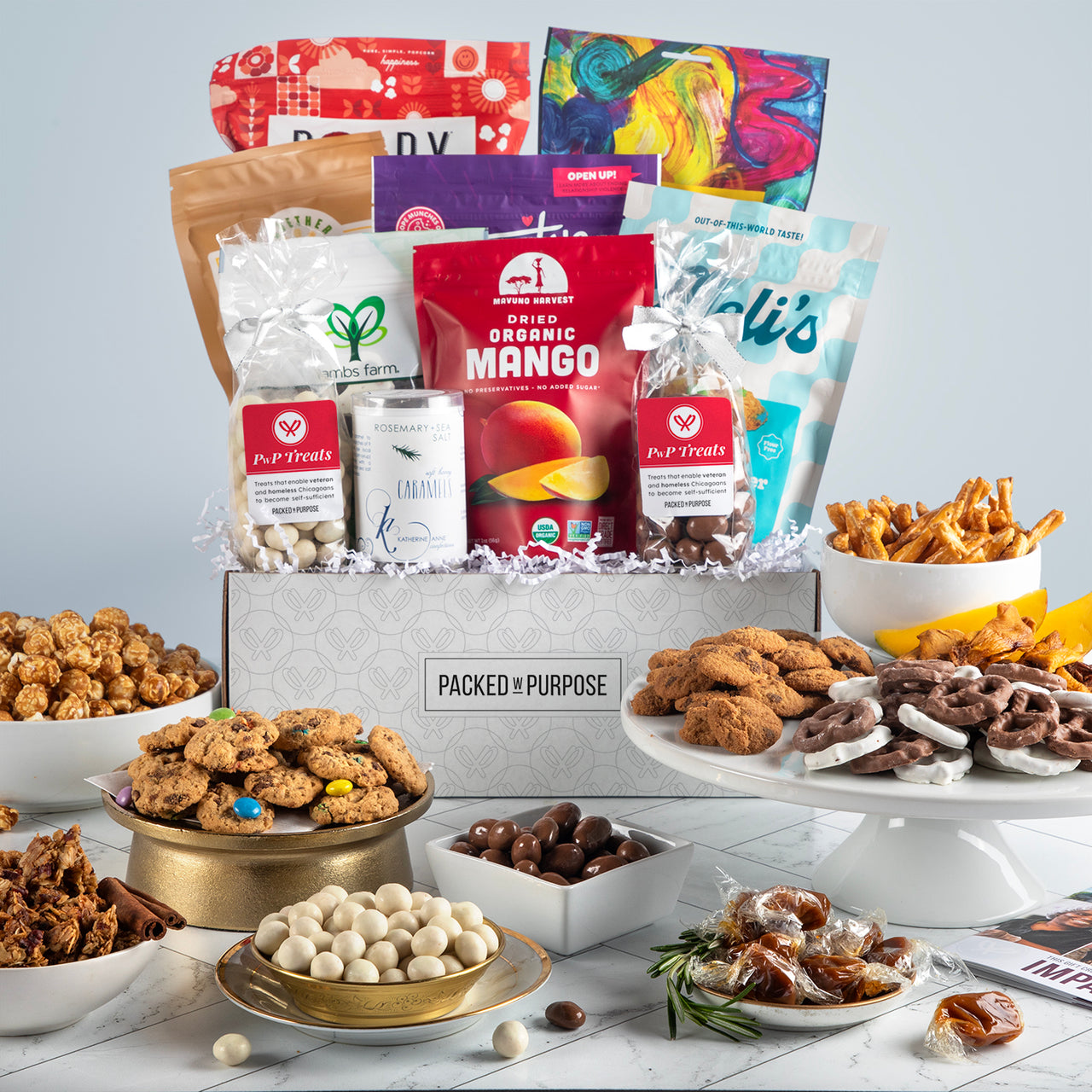 Open gift basket labeled ‘Inspirational Impact’ with chocolate bark, caramels, cookies, popcorn, tea, and honey.