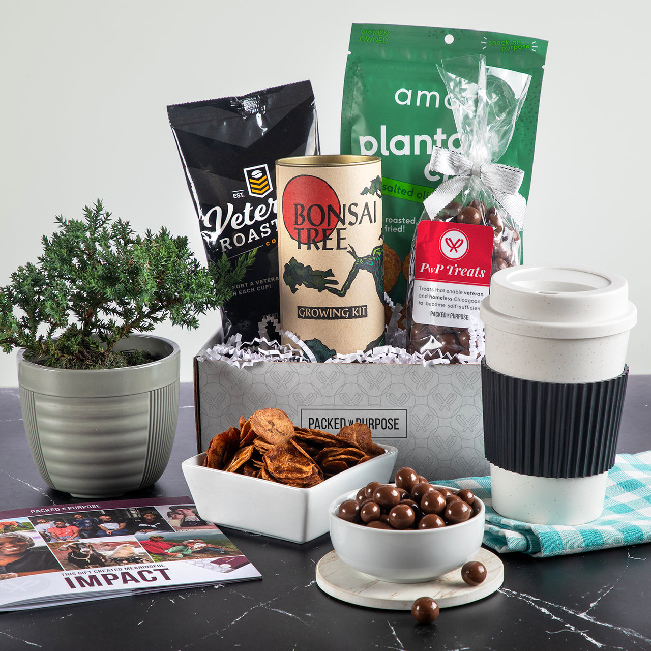 Open gift basket labeled ‘Positive Vibes’ with terrazzo mug, organic tea, chocolate meltaways, jam, and bonsai grow kit.